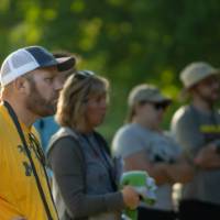 five adults standing outside in the sun listening
